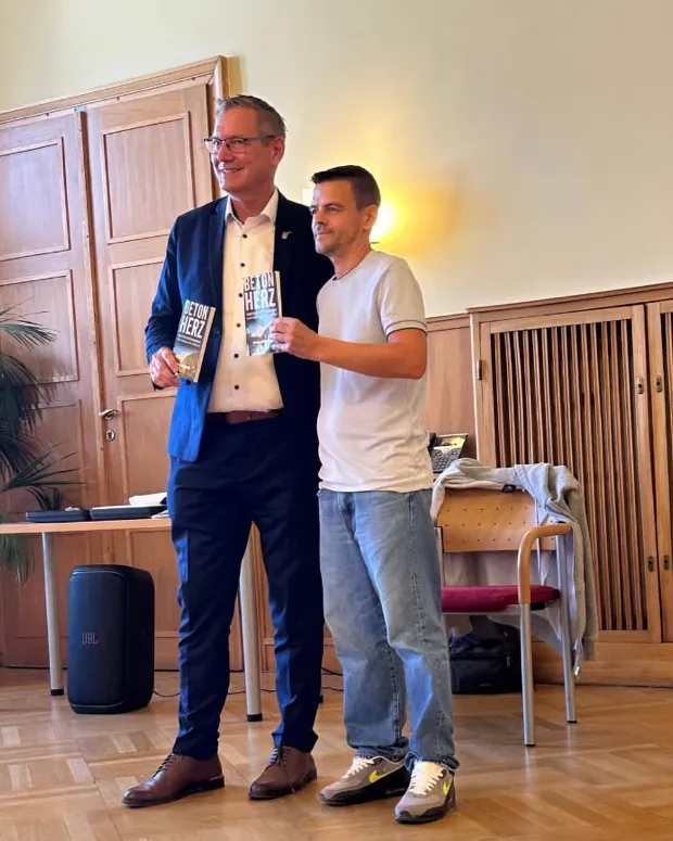Bezirksvorsteher Georg Papai und Michael Stehlik halten bei der Buchpräsentation im Amtshaus Floridsdorf je ein Exemplar von „Beton Herz“